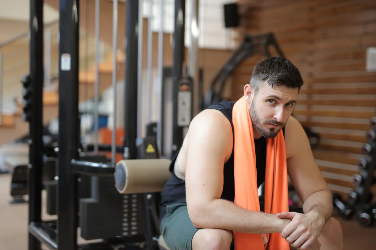 Homme assis dans une salle de sport, serviette orange autour du cou, qui récupère après l'entraînement