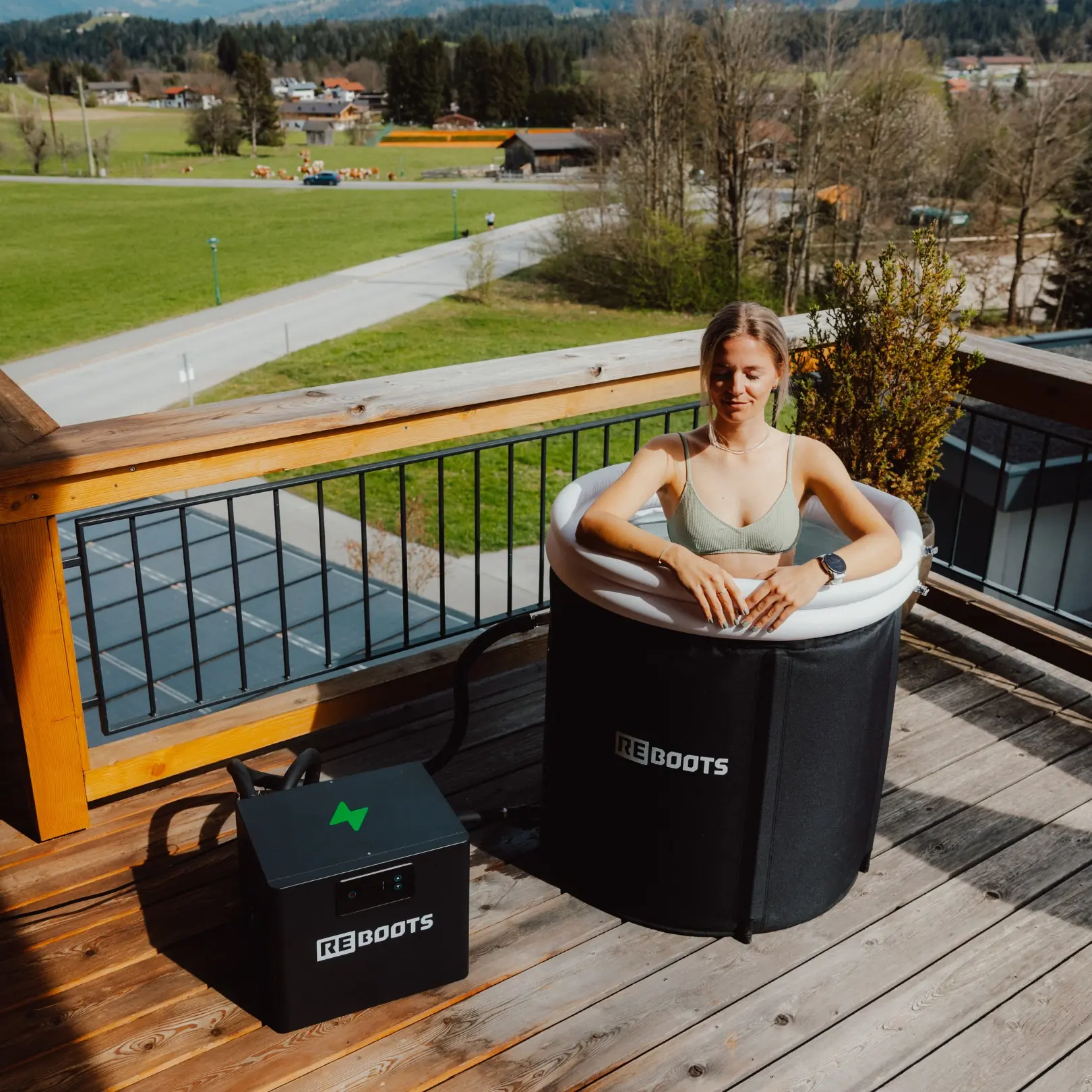 Femme dans l'Ice Tub Pro de Reboots relié à son groupe froid, sur une terrasse en bois face aux montagnes