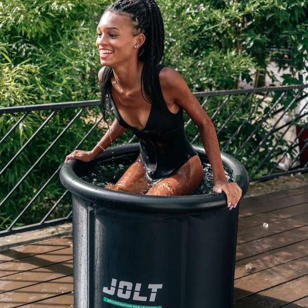 Femme souriante qui entre dans la cuve JOLT Ice Bath, les mains sur le rebord gonflable