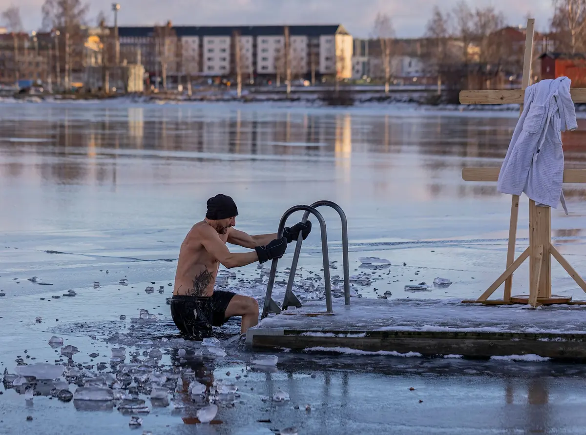 Homme torse nu immergé dans un lac gelé, glace brisée autour de lui, en Suède