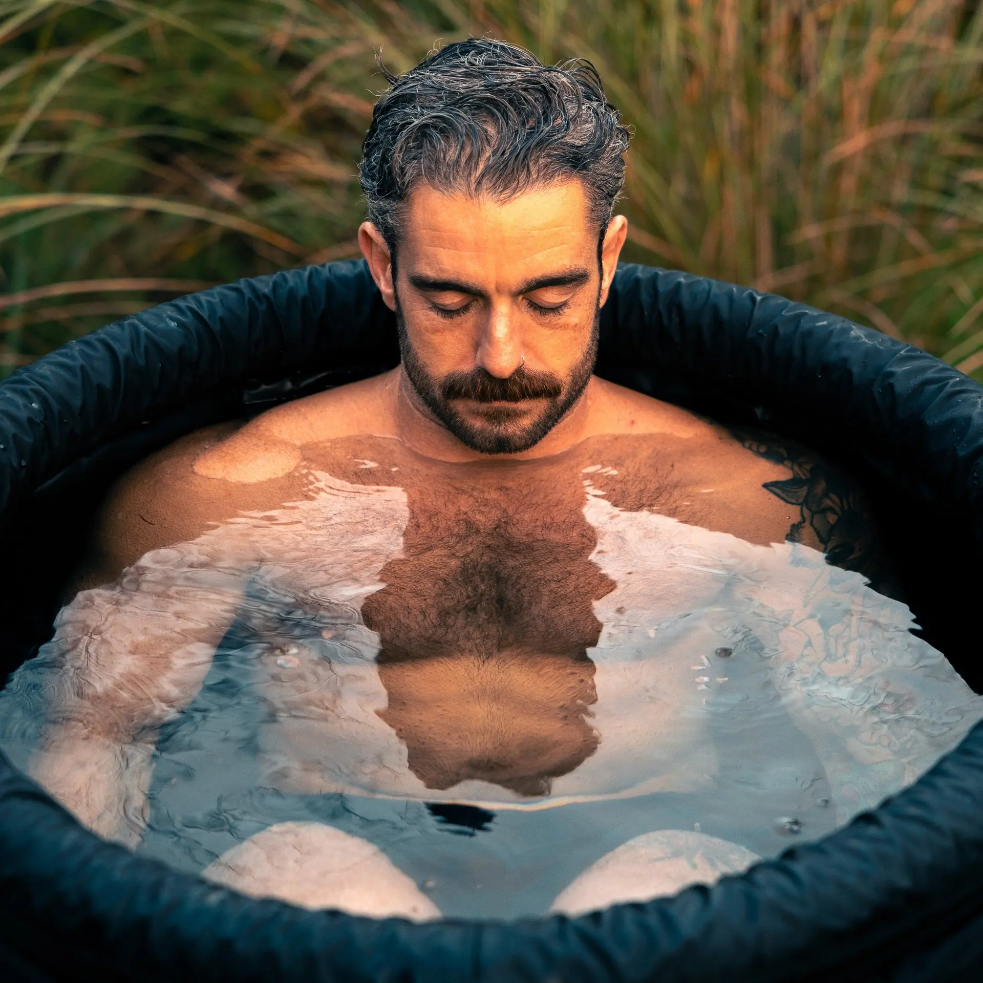 Homme immergé jusqu'à la poitrine dans une cuve LUMI remplie d'eau et de glaçons, végétation en arrière-plan