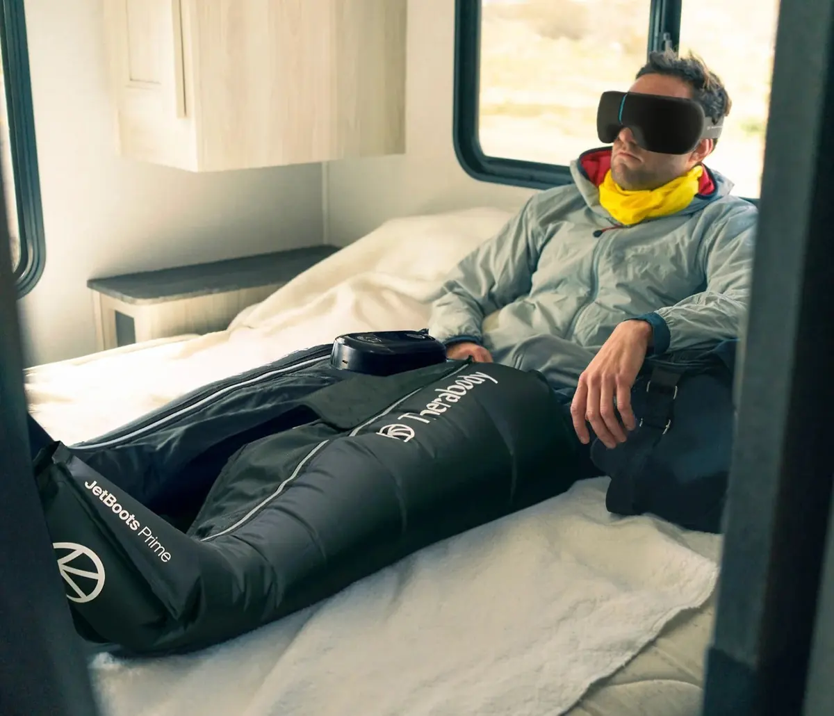 Homme allongé dans un fourgon aménagé, les jambes dans des bottes JetBoots Prime, masque sur les yeux, lumière du jour